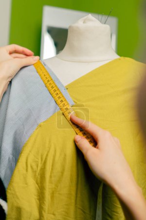 close up in a sewing workshop a seamstress works with a mannequin on a blue fabric measures with a centimeter