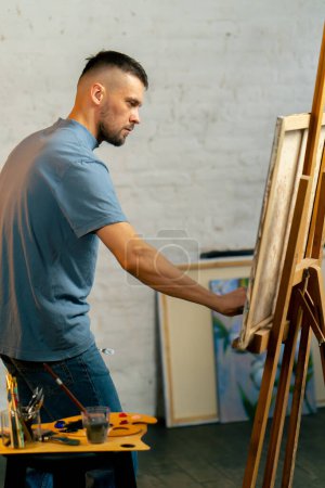 Téléchargez les photos : Dans un atelier d'art un artiste en T-shirt bleu fait une large course avec un couteau de palette - en image libre de droit