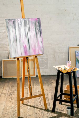 Photo for In the art workshop there is a tripod with a finished painting next to a stool on which there is a palette and brushes - Royalty Free Image