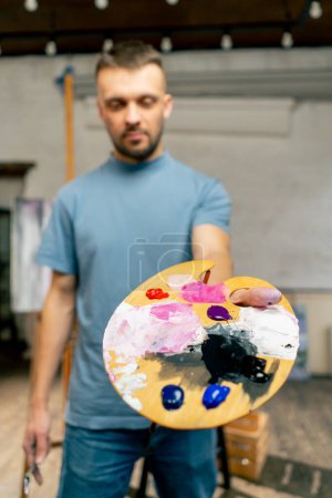 Téléchargez les photos : Dans un studio d'art, un artiste se tient directement à la caméra et montre une palette et - en image libre de droit