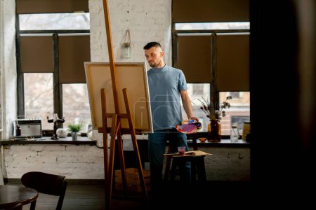 Photo for General shot young artist in a blue t-shirt in an art studio working on a painting - Royalty Free Image