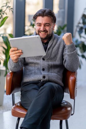 un joven trabajador de oficina en el fondo de una ventana sentado en una silla de trabajo con una sensación de tableta de vencedor