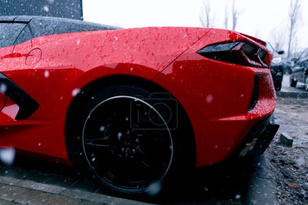 Foto de Primer plano de la espalda con la rueda de un coche deportivo rojo de pie en la calle mojado después de la nieve - Imagen libre de derechos