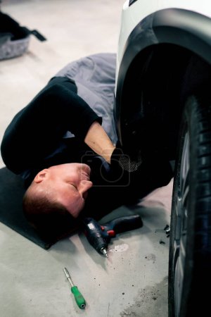 Photo for Close-up of a lying auto mechanic at a service station repairing part of a wheel panel - Royalty Free Image