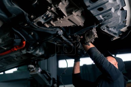 Photo for Auto mechanic at a service station checks the car being lifted on a lift - Royalty Free Image