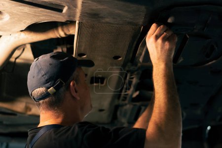 Téléchargez les photos : Dans une station-service, un mécanicien insère un panneau métallique sous la voiture. - en image libre de droit