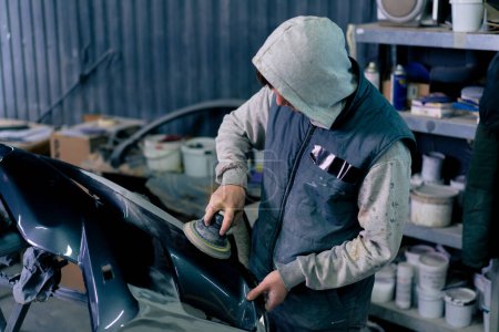 Photo for Auto mechanic at a service station polishing the front part of a dark blue car - Royalty Free Image