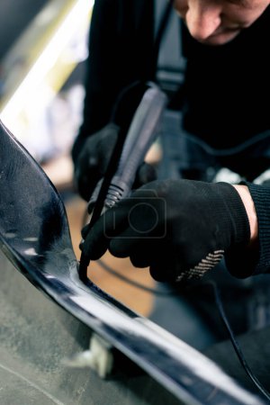 Téléchargez les photos : Fermer Dans une station-service, un mécanicien soude un joint en caoutchouc sur une partie métallique de la voiture - en image libre de droit