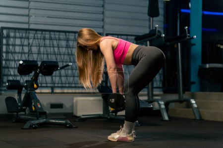 Photo for In the gym a girl in a pink top lifts a barbell and shakes her legs and arms - Royalty Free Image