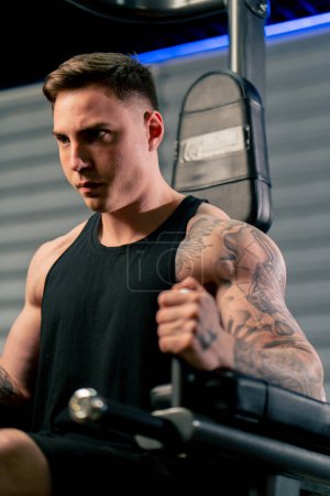 Foto de De cerca en el gimnasio un joven guapo con tatuajes bombea sus abdominales en la barra horizontal - Imagen libre de derechos