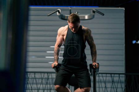 Photo for In the gym young handsome guy with tattoos pulls himself up and pumps his arms on the horizontal bar - Royalty Free Image