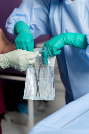 Téléchargez les photos : Dans la salle d'opération en gants verts sort les ciseaux d'un emballage stérile - en image libre de droit