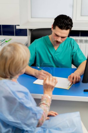 Téléchargez les photos : Gros plan dans une clinique de chirurgie plastique un médecin consulte une femme âgée prenant des notes sur papier - en image libre de droit