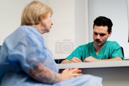Téléchargez les photos : Dans une clinique de chirurgie plastique, un médecin consulte une femme âgée en prenant des notes sur papier - en image libre de droit