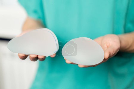Téléchargez les photos : Gros plan dans une clinique de chirurgie plastique un médecin tient deux implants différents dans ses mains - en image libre de droit