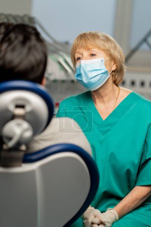 Photo for In a dental clinic young guy patient consults with a female dentist in a green uniform - Royalty Free Image