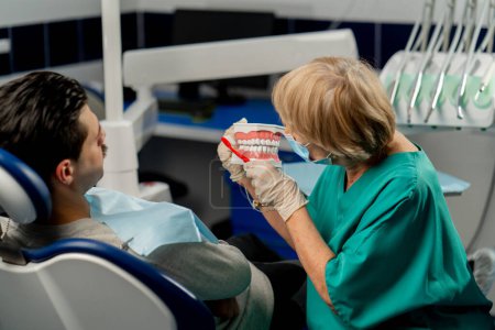 Photo for In a dental clinic a dentist shows a patient how to brush his teeth correctly - Royalty Free Image