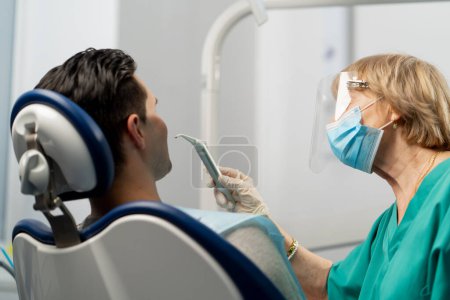 Téléchargez les photos : Dans une clinique dentaire, un orthodontiste souffle des dents pour examiner la cavité buccale. - en image libre de droit