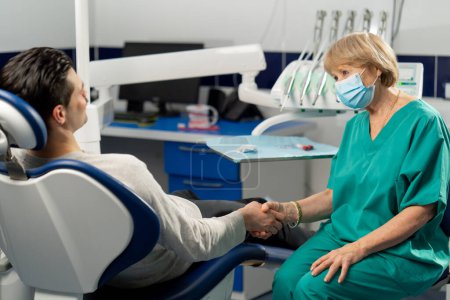 Foto de En la clínica dental el dentista y el paciente se dan la mano alegremente - Imagen libre de derechos