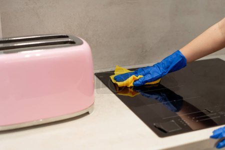 Téléchargez les photos : Gros plan d'un travailleur de l'assainissement les mains dans des gants bleus essuyant un poêle de cuisine avec un chiffon jaune - en image libre de droit