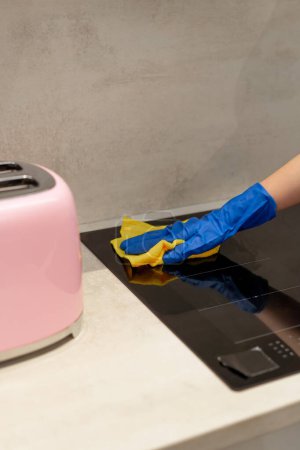 Téléchargez les photos : Gros plan d'un travailleur de l'assainissement les mains dans des gants bleus essuyant un poêle de cuisine avec un chiffon jaune - en image libre de droit