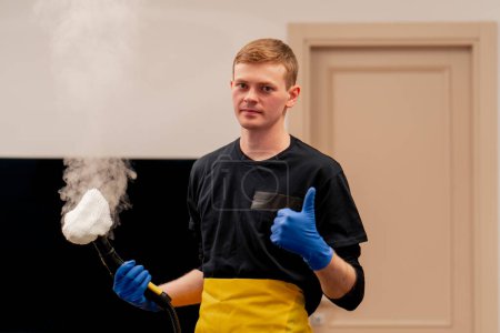 Photo for In the apartment cleaner in a yellow apron stands with a steam generator in his hand super finger to us - Royalty Free Image