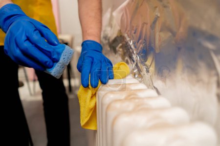 Téléchargez les photos : Fermer dans un appartement un nettoyeur dans un tablier jaune lave une batterie de fer blanc de la rouille - en image libre de droit