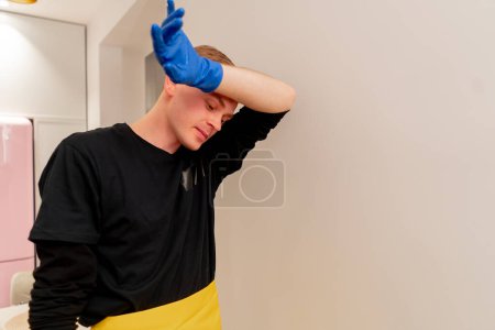 Téléchargez les photos : Close up in the apartment cleaner in yellow apron is tired wiping his forehead from sweat standing near the battery - en image libre de droit