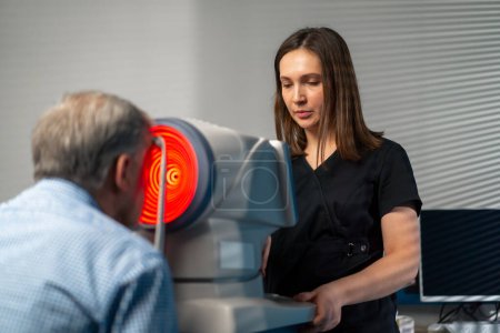 Foto de En una clínica de oftalmología, una doctora realiza un diagnóstico usando un dispositivo con luz roja - Imagen libre de derechos