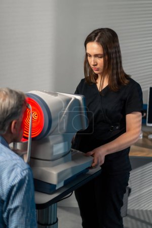 Photo for In an ophthalmology clinic a female doctor performs a diagnosis using a device with a red light - Royalty Free Image
