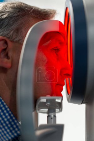 Téléchargez les photos : Gros plan dans la clinique d'ophtalmologie patient âgé est diagnostiqué avec un test de vision à l'aide d'une machine à lumière rouge - en image libre de droit
