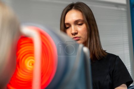 Photo for Close up in an ophthalmology clinic a female doctor performs diagnostics using a device with red - Royalty Free Image