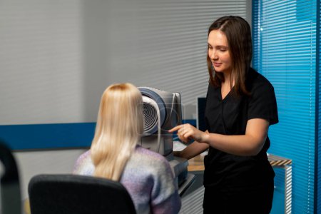 Photo for In an ophthalmology clinic a woman doctor shows a girl with her finger how to tighten the skin under the eye - Royalty Free Image