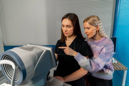 Téléchargez les photos : Dans une clinique d'ophtalmologie femme médecin montre la patiente et dit les résultats du diagnostic montre son doigt - en image libre de droit