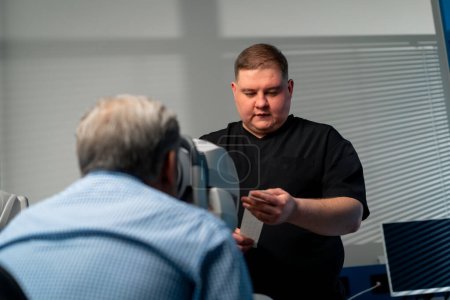 Photo for In an ophthalmology clinic obese doctor looks at diagnostic results on paper - Royalty Free Image