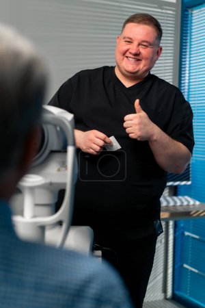 Téléchargez les photos : Dans une clinique d'ophtalmologie un médecin obèse dit que les résultats des diagnostics oculaires sourit avec un super doigt - en image libre de droit