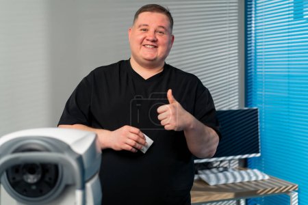 Photo for In an ophthalmology clinic an obese doctor says the results of eye diagnostics smiles with a super finger - Royalty Free Image
