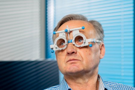 Foto de Primer plano en una clínica de oftalmología paciente de edad avanzada selecciona una lente comprueba la visión leyendo - Imagen libre de derechos
