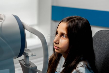 Téléchargez les photos : Gros plan dans une clinique d'ophtalmologie une petite fille diagnostiquera la vision avec une machine à lumière rouge - en image libre de droit