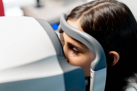 Foto de Primer plano en una clínica de oftalmología una niña pequeña diagnostica la visión con una máquina de luz roja - Imagen libre de derechos