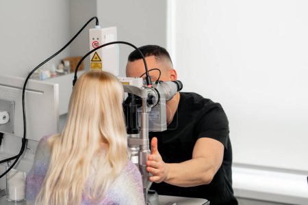 Foto de En una clínica de oftalmología, un médico joven diagnostica a una niña con una lupa - Imagen libre de derechos
