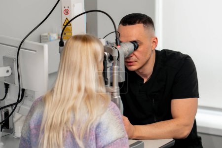 Photo for In an ophthalmology clinic young doctor diagnoses a young girl with a magnifying lens - Royalty Free Image
