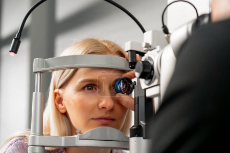 Téléchargez les photos : Gros plan dans une clinique d'ophtalmologie un jeune médecin diagnostique les yeux d'une jeune fille avec une loupe - en image libre de droit