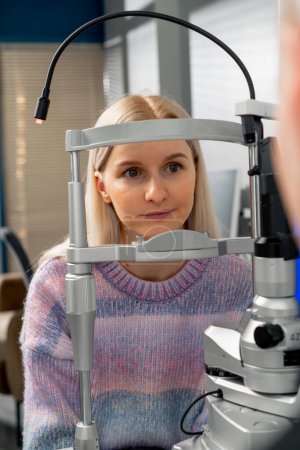 Téléchargez les photos : Dans une clinique d'ophtalmologie, une jeune fille communique avec un médecin au moyen d'une machine de diagnostic - en image libre de droit