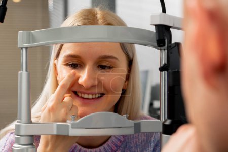 Téléchargez les photos : Fermer dans une clinique d'ophtalmologie une jeune fille communique avec un médecin grâce à une machine de diagnostic regarder sur le doigt - en image libre de droit