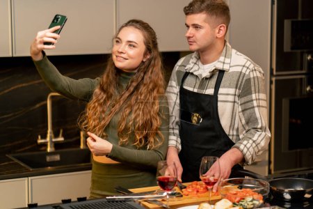 Téléchargez les photos : Jeune couple amoureux dans une belle cuisine préparant le dîner ensemble et prenant des photos - en image libre de droit