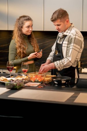 Téléchargez les photos : Jeune couple amoureux dans une belle cuisine préparer le dîner ensemble la fille photographie la nourriture - en image libre de droit