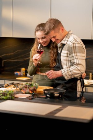 Photo for Young couple in love in beautiful kitchen preparing dinner together and drinking wine - Royalty Free Image
