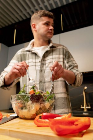 guy in love in the kitchen stirring Greek salad preparing a romantic dinner