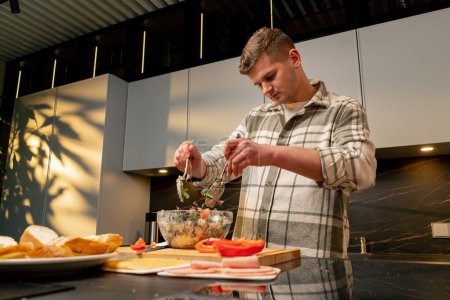 Téléchargez les photos : Guy in love in the kitchen stirring Greek salad preparing a romantic dinner - en image libre de droit